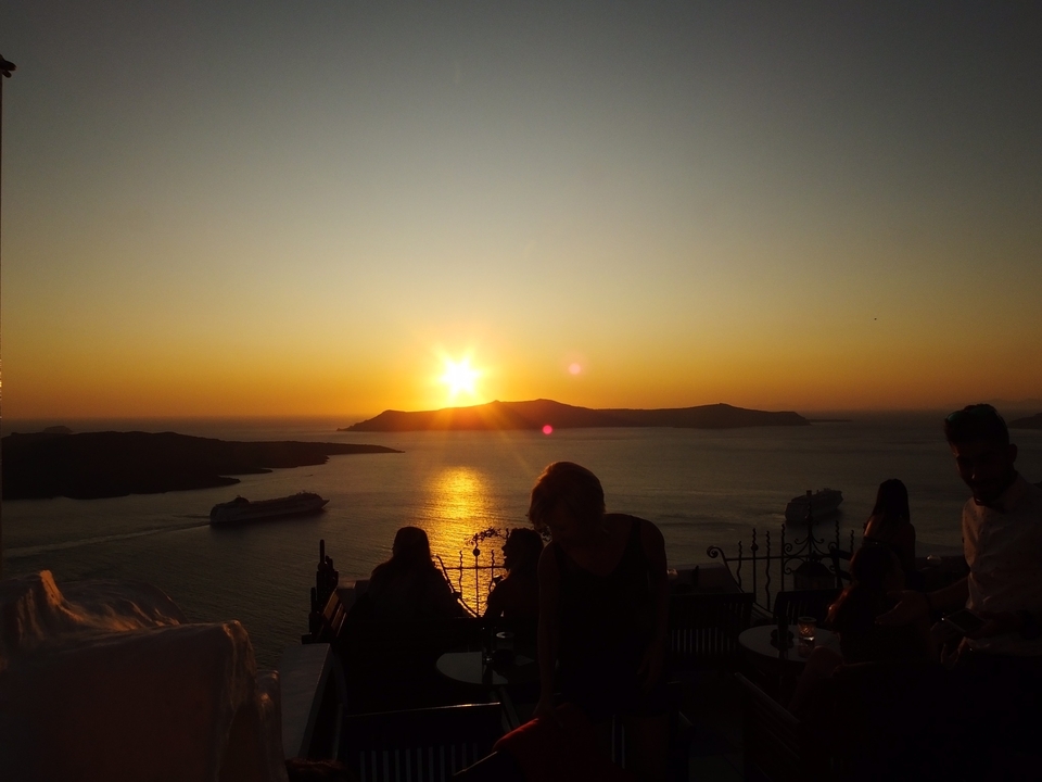 Des gens qui profitent d'un coucher de soleil sur l'océan depuis une terrasse.