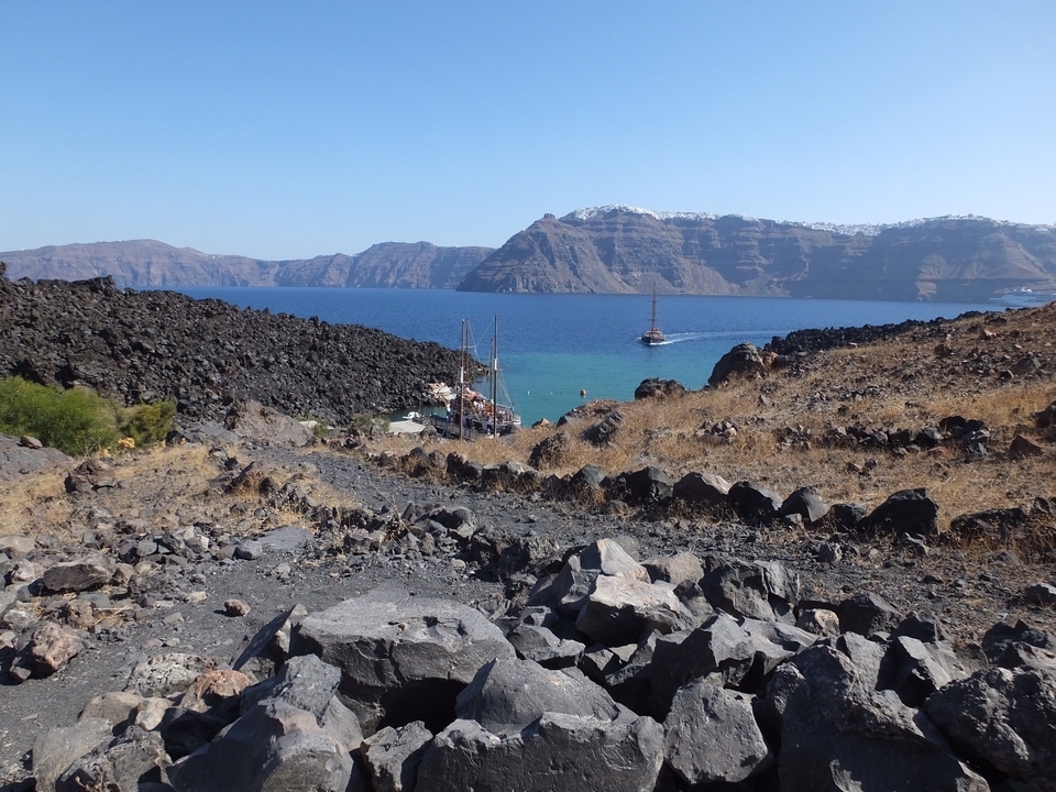 Paysage rocheux avec des bateaux en mer et des montagnes au loin.