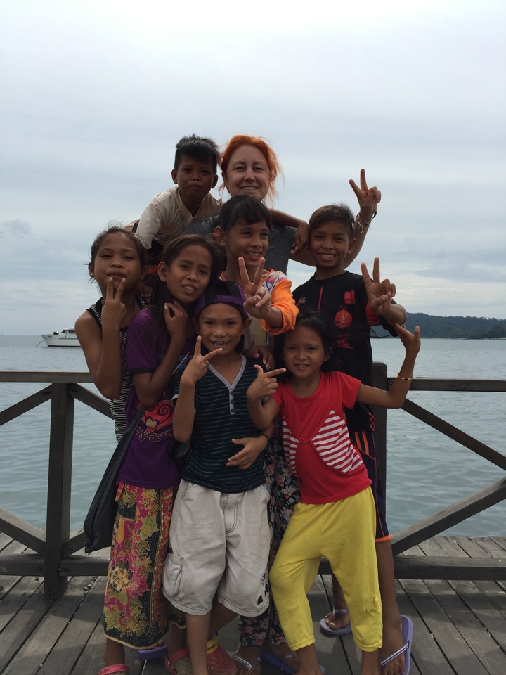 Groupe d'enfants posant sur une jetée avec de l'eau et un bateau en arrière-plan.