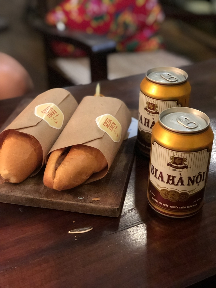 Bánh mì et canettes de bière brassée localement sur une table en bois.