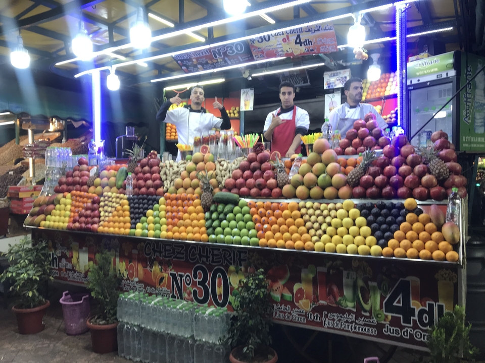 Étal coloré de fruits et de jus sur un marché avec des gens.