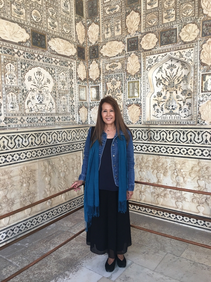 Personne posant dans une salle de marbre ornée avec des motifs floraux détaillés.