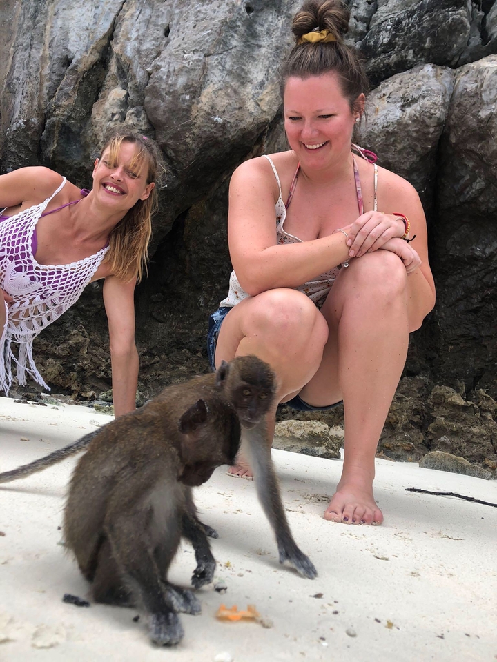 Deux personnes posant avec un singe sur une plage.