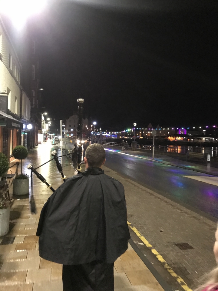 Rue la nuit avec un joueur de cornemuse marchant le long du trottoir.