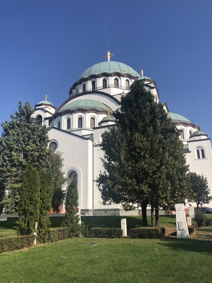 Grande église blanche avec des dômes verts entourée d'arbres.