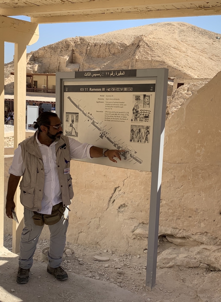 Une guide expliquant une carte dans un site antique.
(or alternatively: Un guide expliquant une carte dans un site antique.)
Note: In French, "guide" can be either masculine (un guide) or feminine (une guide) when referring to a person who gives guided tours. Both forms are correct.