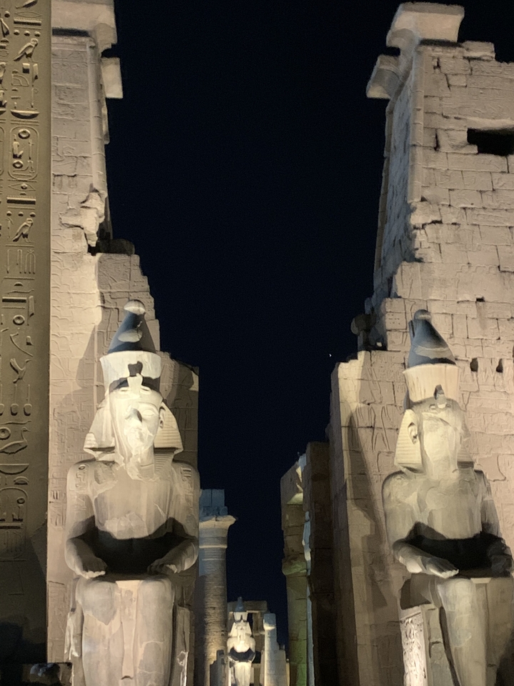 Statues illuminées et ruines antiques la nuit.