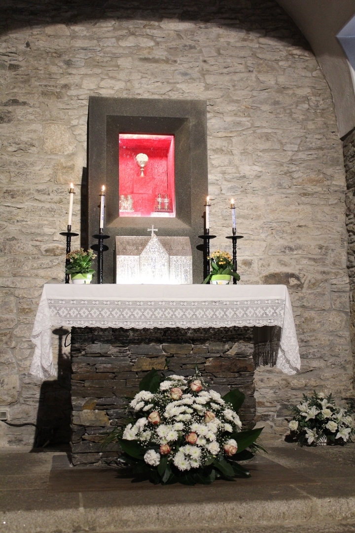 Autel intérieur avec bougies allumées, fleurs et figurines religieuses.