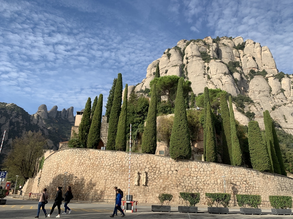 Des cyprès bordent une colline avec en toile de fond la montagne de Montserrat.
