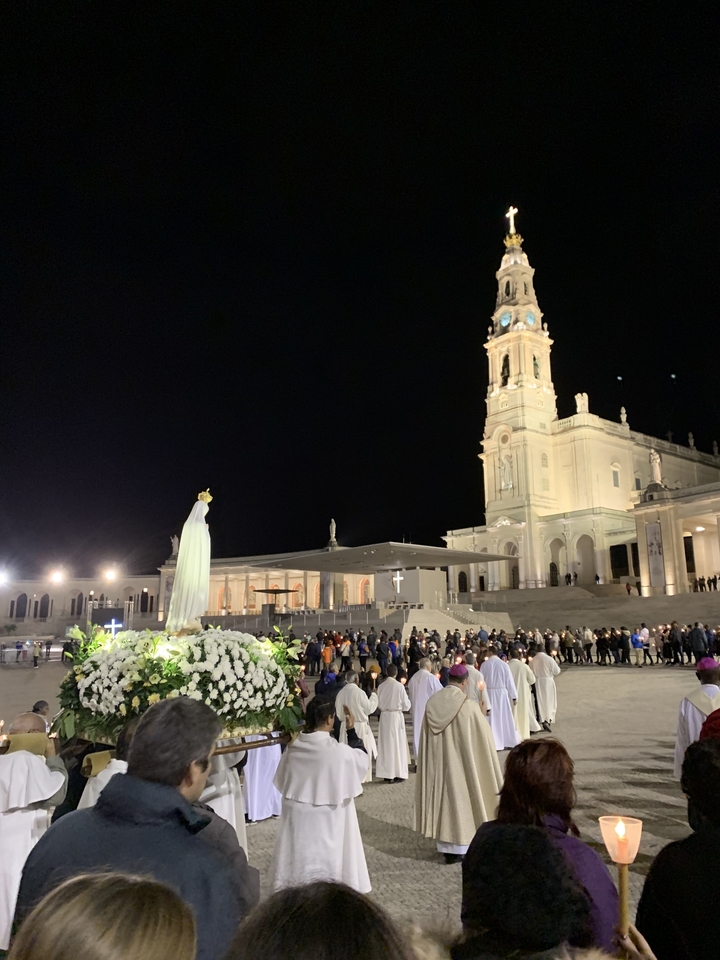 Vue nocturne d'un complexe religieux avec statue éclairée et foule.