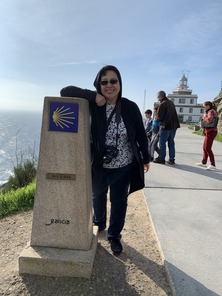Personne s'appuyant sur un marqueur indiquant le point d'arrivée du Chemin de Saint-Jacques-de-Compostelle.