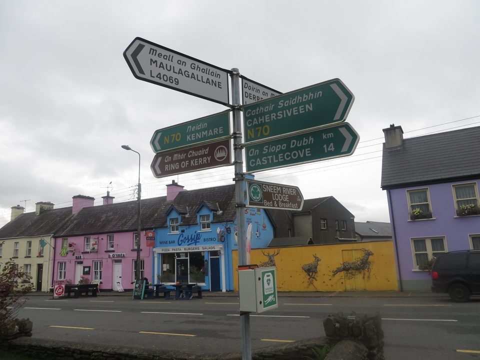 Rue avec des maisons colorées et des panneaux routiers indiquant les destinations.