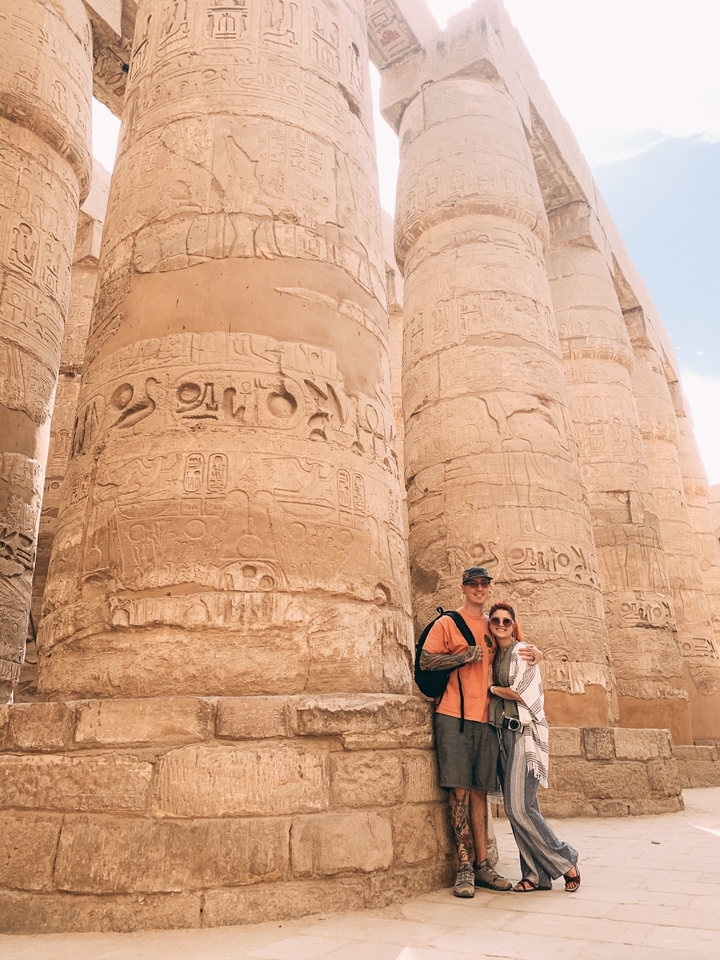 Couple posant devant des colonnes de temple égyptien antique avec des hiéroglyphes.