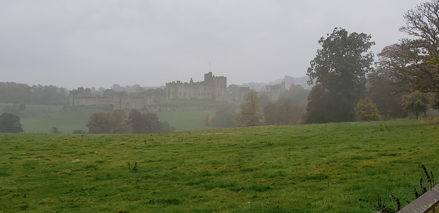 Vista lejana de un castillo en un día brumoso con campos verdes.