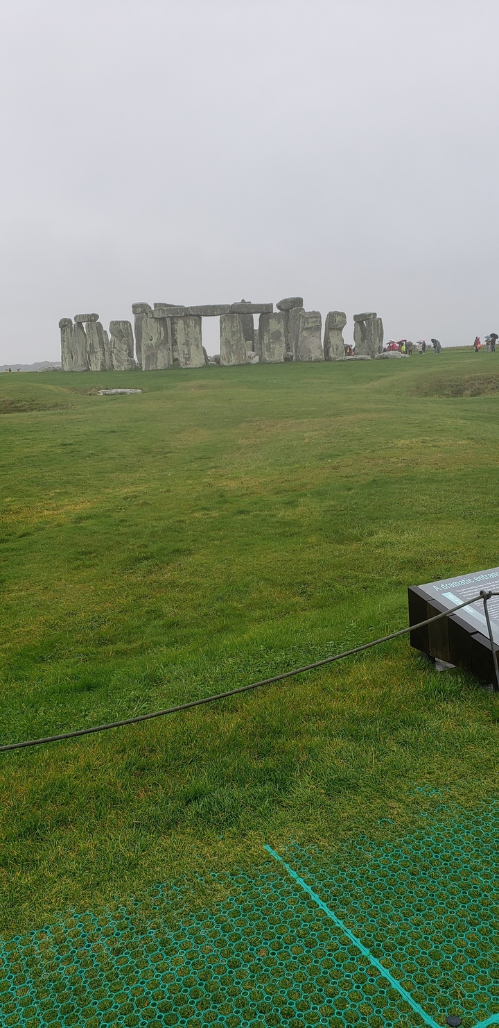 Campos verdes con una vista distante de colinas y una pequeña roca.