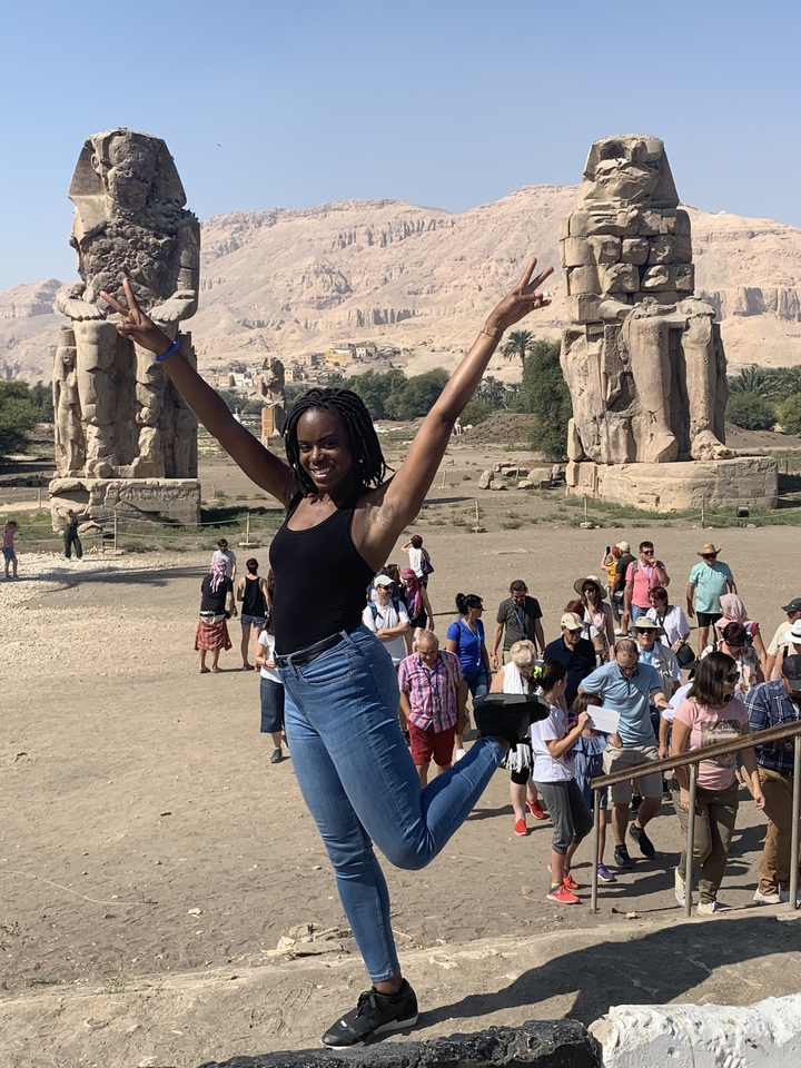 Une femme posant joyeusement avec des statues anciennes en arrière-plan.