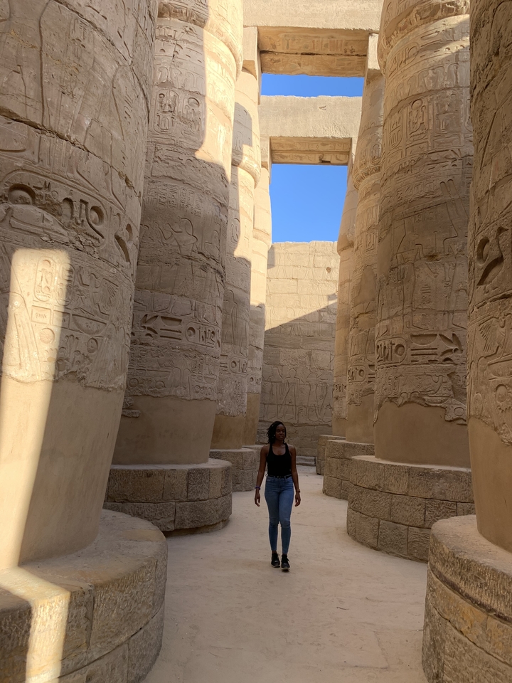 Une personne se tenant parmi les colonnes de pierre massives avec des hiéroglyphes.