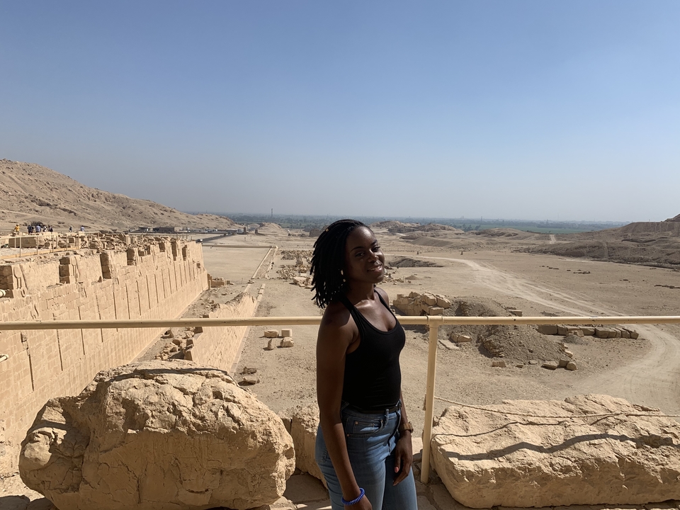 Une femme posant devant un vaste site archéologique désertique.
