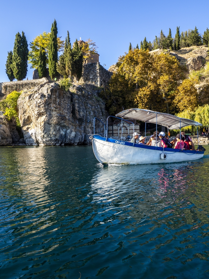 Un petit bateau avec des touristes sur un lac calme entouré de falaises.