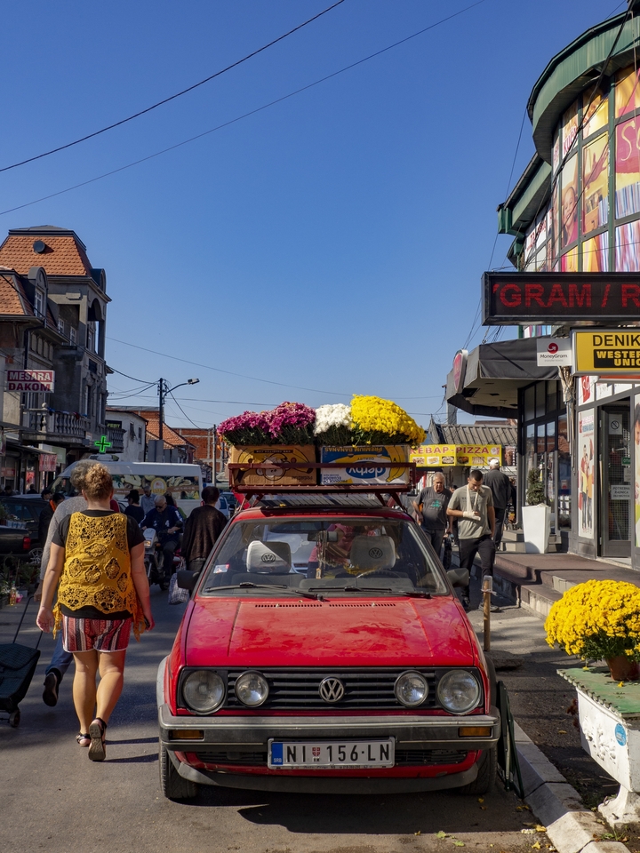 Une rue animée avec une voiture transportant des fleurs sur son toit.