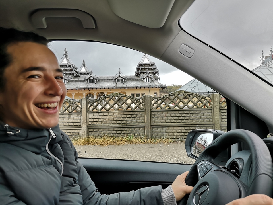 Une femme souriante dans une voiture avec un bâtiment orné à l'extérieur.
