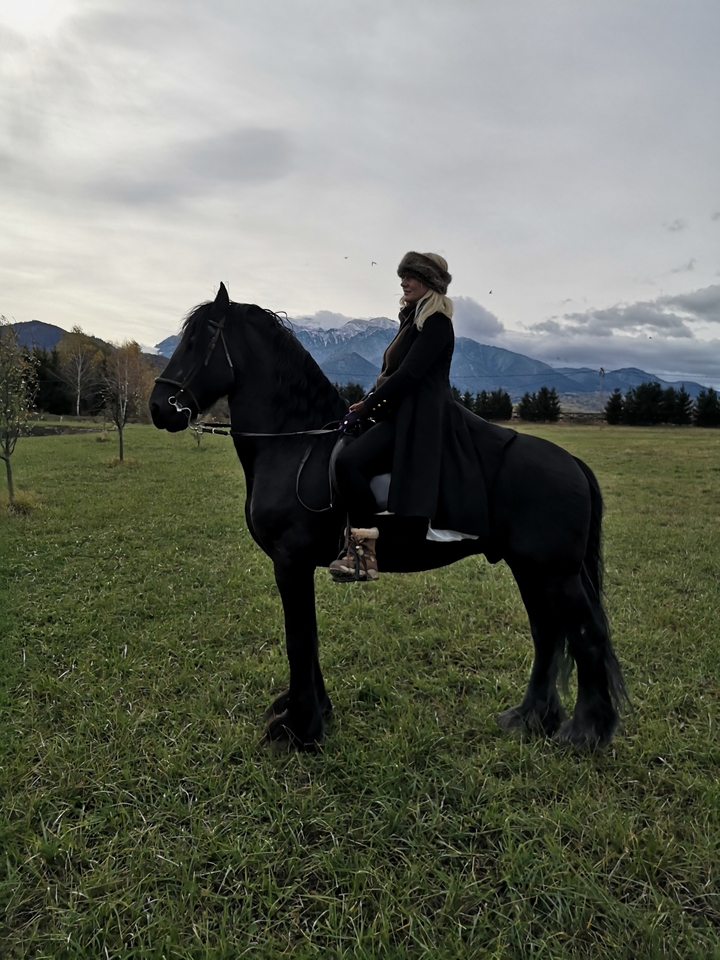 Une femme sur un cheval posant dans un champ pittoresque avec des montagnes.