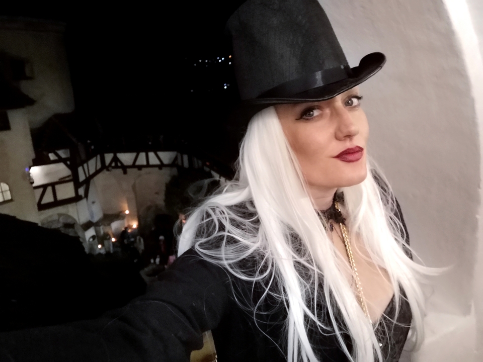 Une femme qui pose à l'intérieur avec un costume, portant un chapeau.