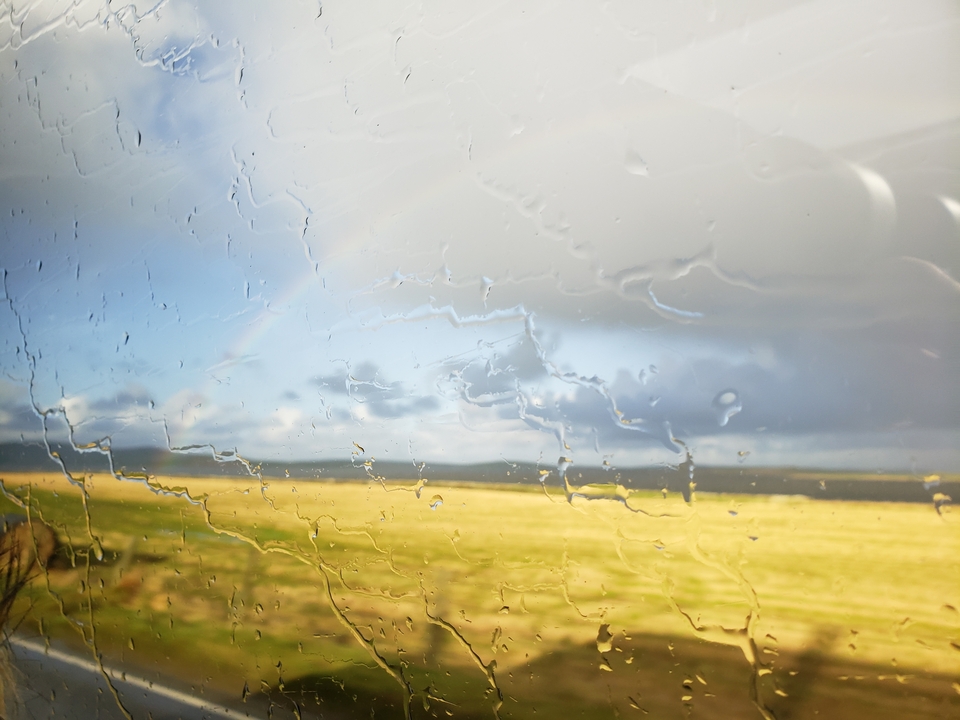 Vue à travers une fenêtre pluvieuse avec des champs et un arc-en-ciel