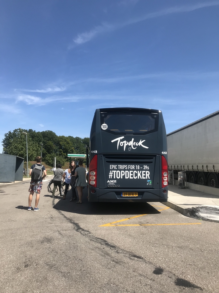 Un autobus avec sa marque où des gens montent à bord, sous un ciel ensoleillé.