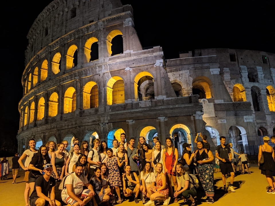 Groupe de personnes posant devant le Colisée illuminé la nuit.