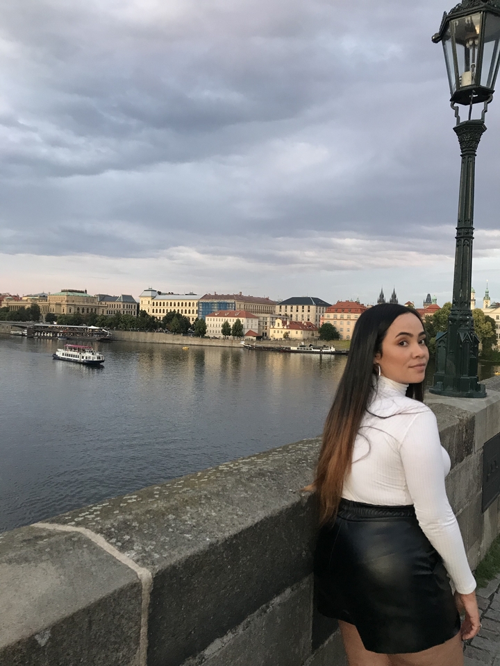 Une personne sur un pont surplombant une rivière avec des bâtiments de la ville et un bateau.