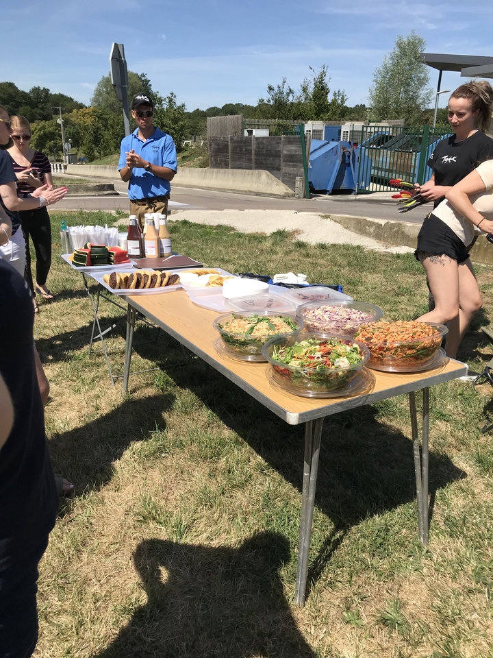 Table de buffet extérieur avec divers plats et des personnes autour.