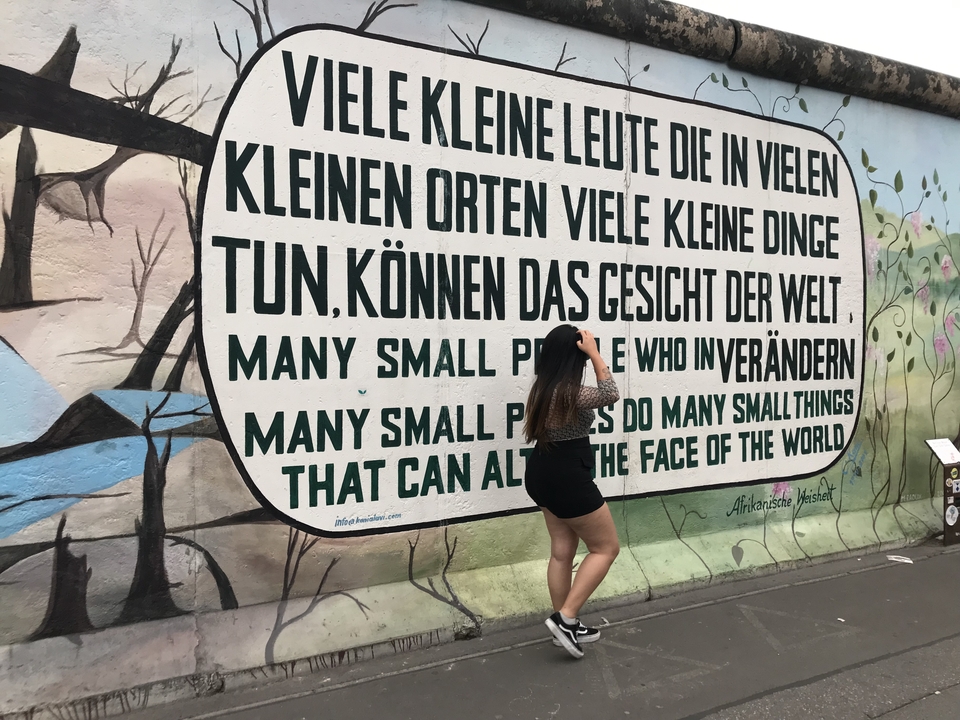 Une personne debout devant une peinture murale avec du texte en deux langues.
