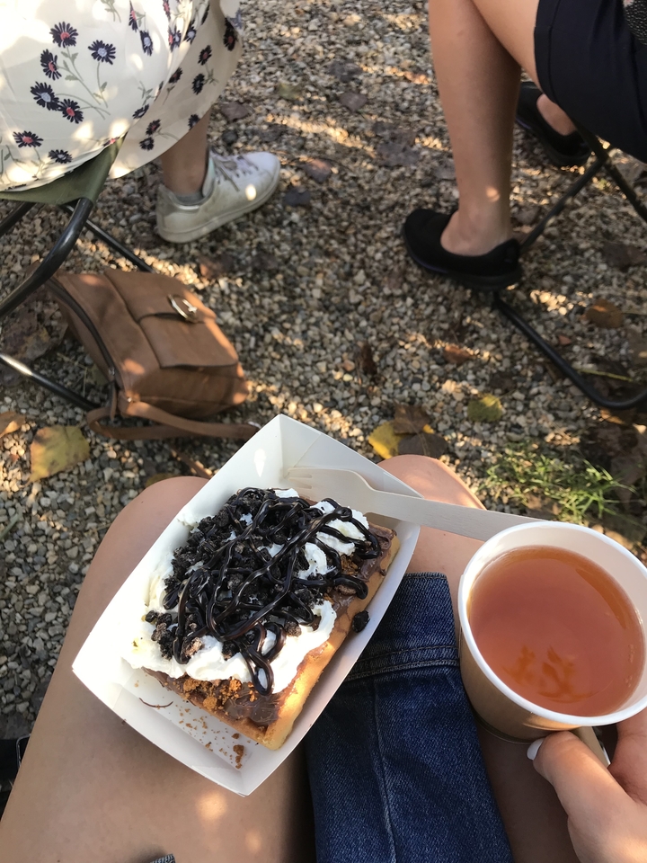 Un dessert avec une sauce au chocolat et une tasse de thé sur les genoux d'une personne dans un cadre de jardin.