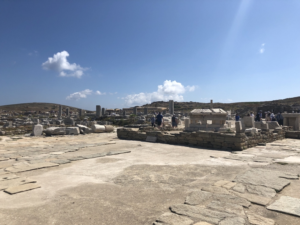 Des gens explorant des ruines antiques sous un ciel lumineux.