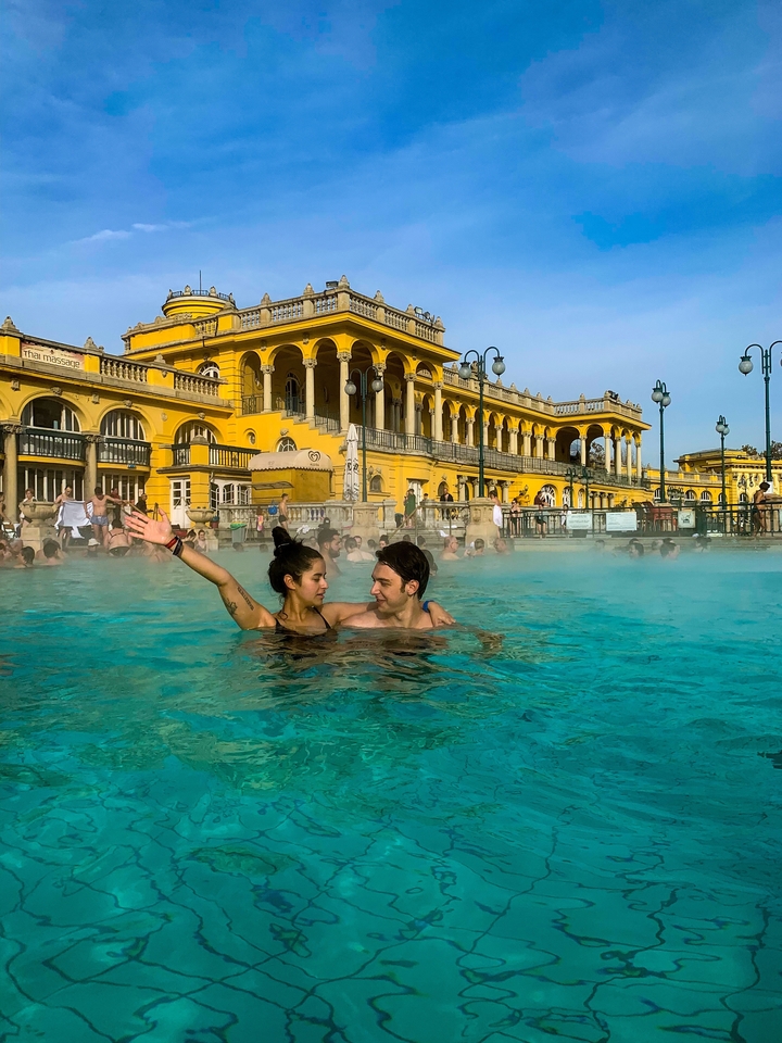 A couple enjoying a thermal bath in front of a historic building.
