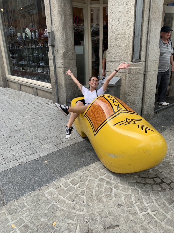 Personne qui rit en étant assise dans un grand sabot en bois dans une rue.