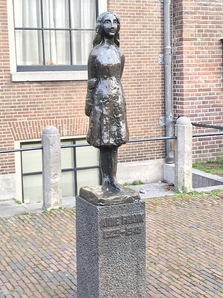 Statue d'une personne en bronze contre un mur de briques.