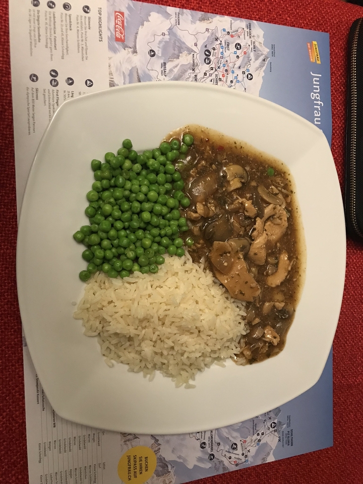 Assiette de nourriture avec des petits pois, du riz et du poulet en sauce.