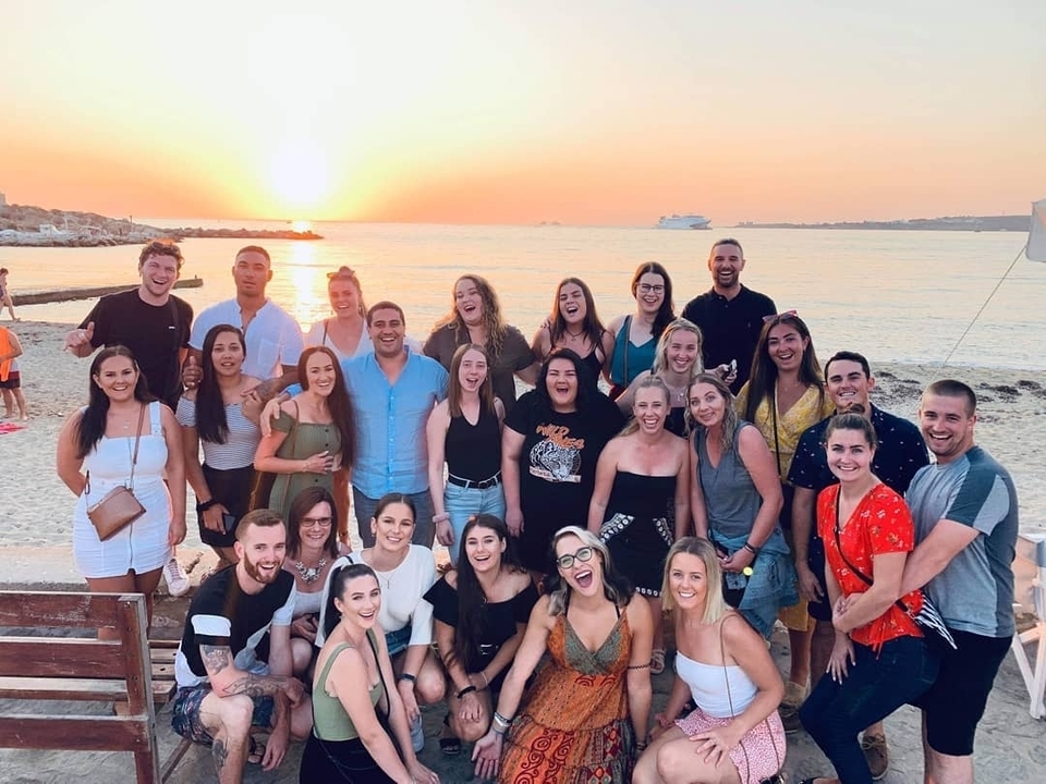 Un groupe de personnes posant au bord de la mer au coucher du soleil.