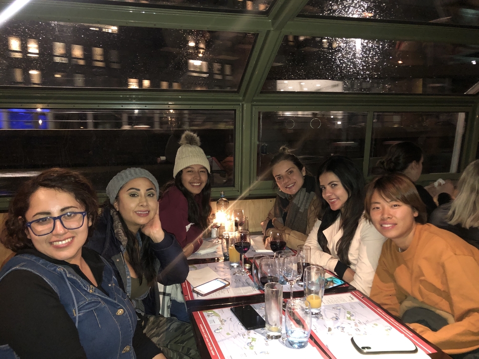 Un groupe de personnes dînant à l'intérieur près d'une fenêtre avec de la pluie visible dehors.