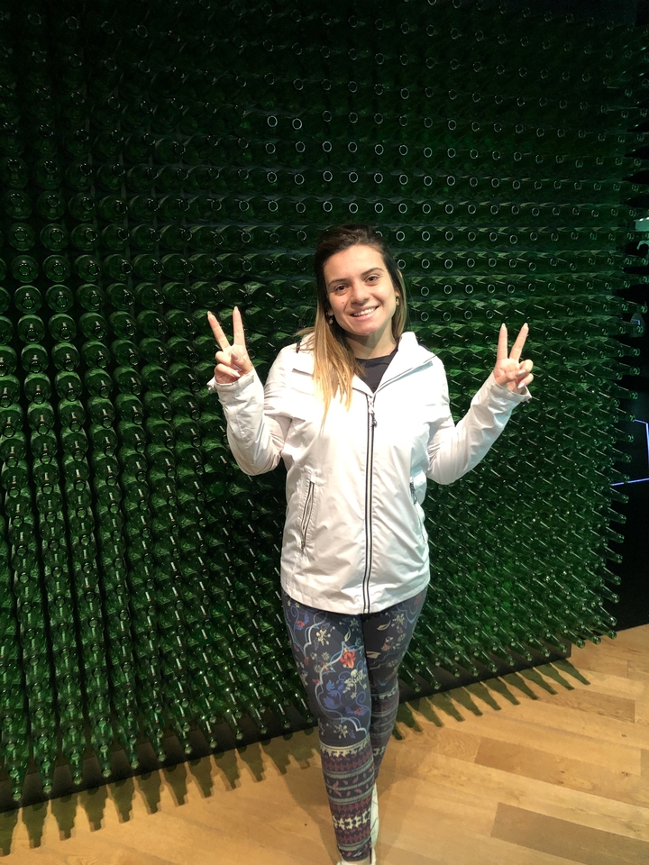 Une personne souriante devant un mur de bouteilles en verre vert.