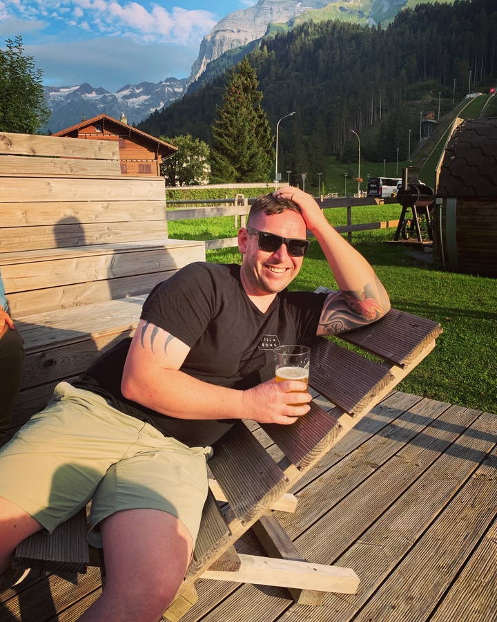 Homme se détendant sur une chaise longue avec une boisson, en plein air.