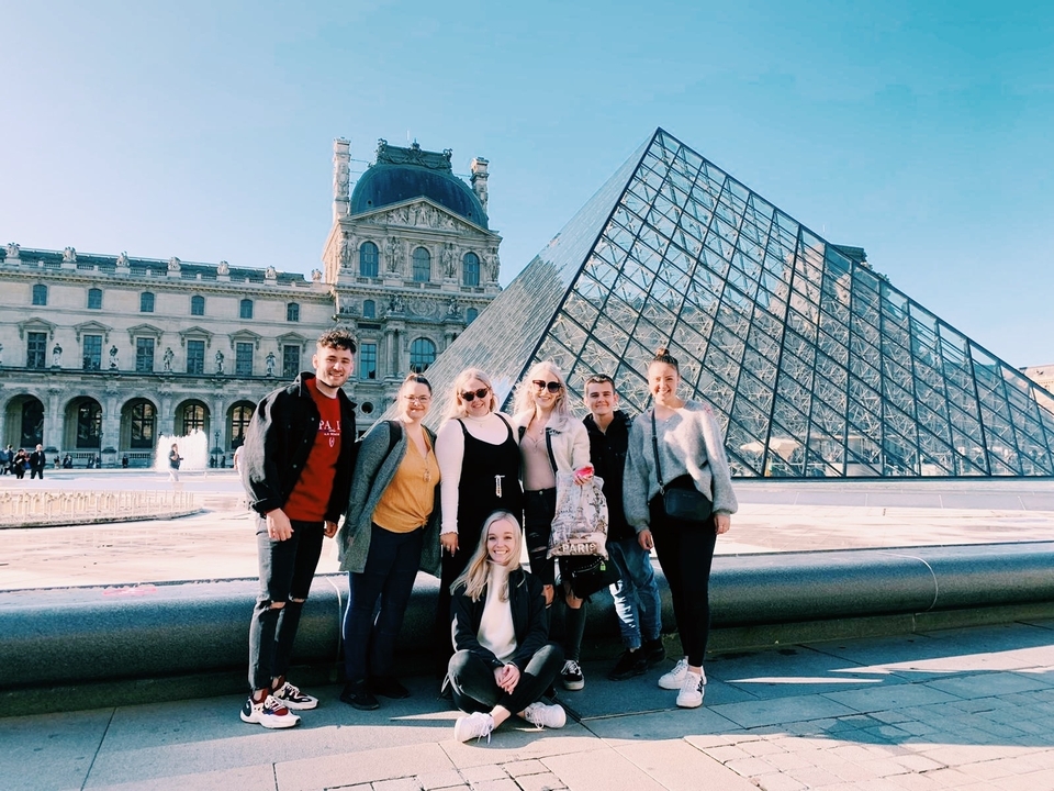 Un groupe de personnes posant devant la Pyramide du Louvre à Paris.