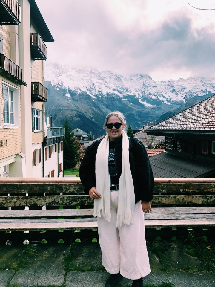Une personne posant avec un village de montagne en arrière-plan, possiblement à Lauterbrunnen.