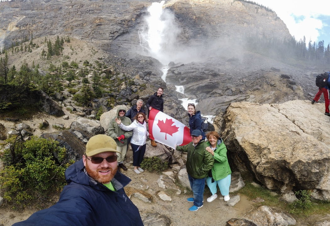 Groupe de personnes avec un drapeau canadien devant une cascade.