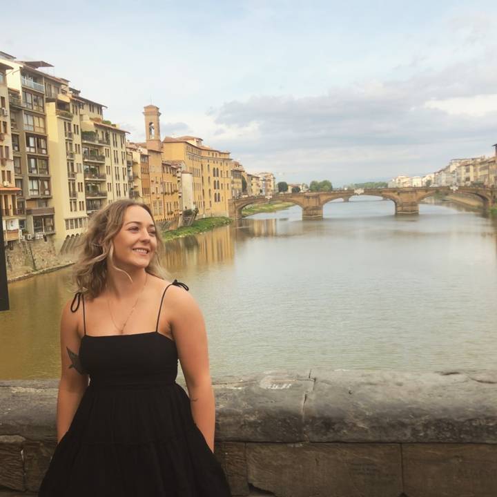 Woman in front of a river and bridges with old buildings.