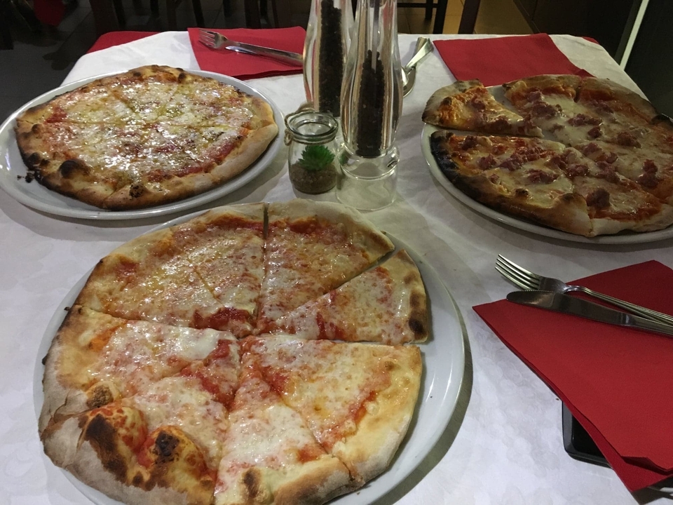 Trois pizzas servies sur une table dressée avec des couverts.