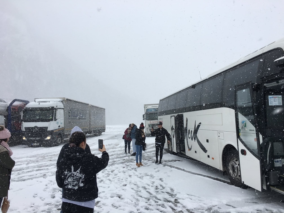 Des touristes prenant des photos au milieu d'une forte chute de neige près de plusieurs autobus stationnés.