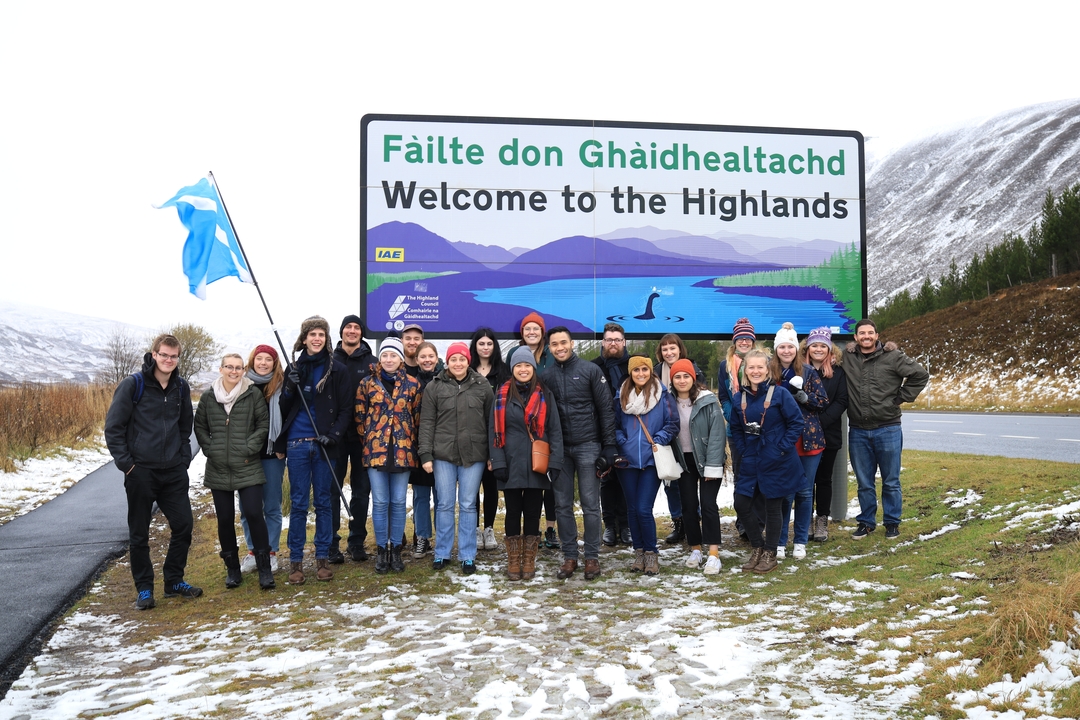 Group of tourists under a sign saying 'Welcome to the Highlands'.